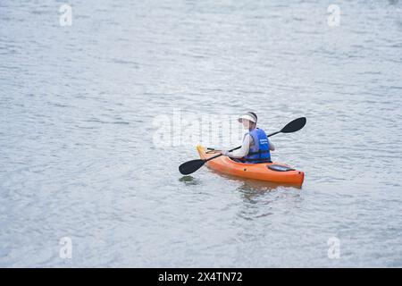 (240505) -- FUZHOU, 5. Mai 2024 (Xinhua) -- Eine junge Frau paddelt mit dem Kajak im Fluss Minjiang in der Stadt Jingxi in der südöstlichen Provinz Fujian, 27. April 2024. Das Oasis Camp in Jingxi Stadt Fuzhou liegt im Minjiang-Flussbecken und ist umgeben von üppigen grünen Bergen und klarem Wasser, was es zu einem beliebten Reiseziel für Outdoor-Wassersport macht. In den letzten Jahren haben sich Motorsurfen, Kajakfahren und Paddleboarding zu den „neuen Favoriten“ für die jungen Menschen hier entwickelt. Auf dem Paddelbrett zu liegen, den blauen Himmel, die weißen Wolken und den Sonnenuntergang zu betrachten, ist auch eine Art von Stockfoto