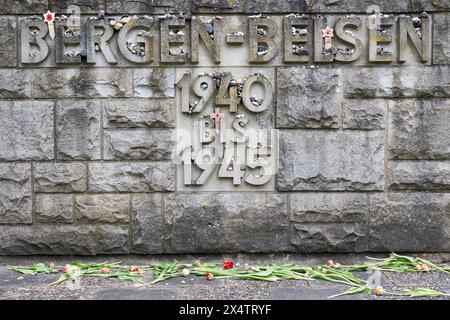 Lohheide, Deutschland. Mai 2024. Die Worte „Bergen-Belsen, 1940 bis 1945“ stehen auf einer Steinmauer auf dem Gelände der Bergen-Belsen Gedenkstätte. Mehrere Blumen liegen davor. Im April 1945 befreiten britische Truppen das Konzentrationslager Bergen-Belsen, wo über 52.000 Menschen starben. Quelle: Michael Matthey/dpa/Alamy Live News Stockfoto