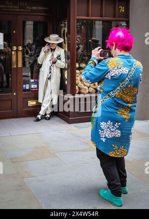 London, Großbritannien. Mai 2024. Ein eleganter Gentleman, der weithin als „Soho George“ bekannt ist, sieht entspannt aus, während er von einer Dame mit rosa Haaren fotografiert wird. Am jährlichen Grand Flaneur Walk nehmen eine Gruppe von elegant gekleideten Jungs, Kapellen und Tänzerinnen Teil, die neben der Statue von Beau Brummell in der Jermyn Street beginnen und dann durch die Londoner St. James' Gegend schlendern. Quelle: Imageplotter/Alamy Live News Stockfoto