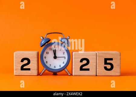 2025, Geschäftskonzept, Symbol für das neue Jahr. Der graue Wecker zählt bis 12. Schöner oranger Hintergrund, Kopierraum. 2025 Happy New Year Stockfoto