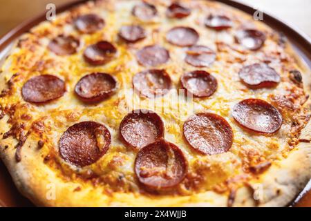 Nahaufnahme einer köstlichen Peperoni-Pizza mit geschmolzenem Käse auf einem braunen Teller Stockfoto