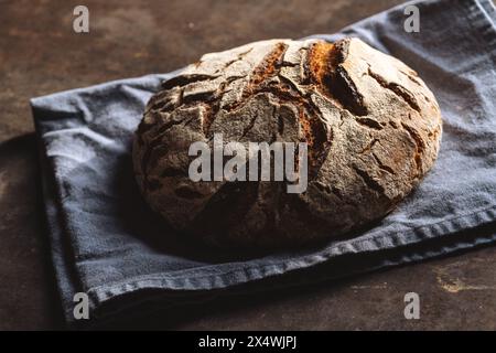 Nahaufnahme eines knusprigen Sauerteigbrotes auf einer blauen Leinenserviette, auf einer dunklen strukturierten Oberfläche Stockfoto