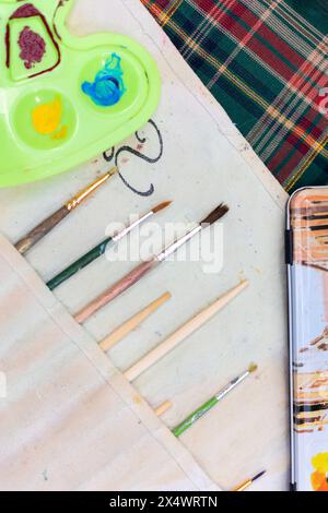 Verschiedene gebrauchte Pinsel mit Palette auf dem Tisch, junge Künstler Objekte Stockfoto