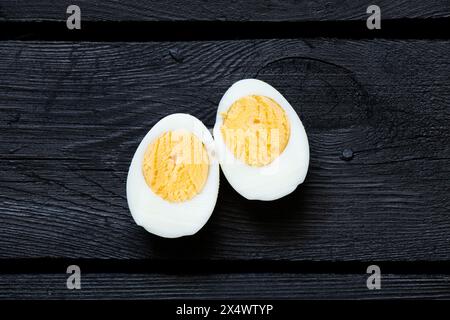 Ein gekochtes Hühnerei, geschnitten, liegt auf einem schwarzen Holzbrett, Essen Stockfoto