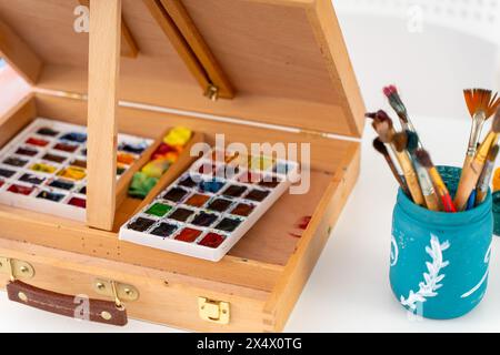 Aquarellfarben und Schwämme zum Malen in einer faltbaren Staffelei und Kunstpinsel in einem Glas. Ausgewählter Fokus. Hochwertige Fotos Stockfoto