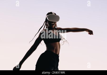 Mädchen tanzt in einem Studio, trägt einen Sport-BH. Sie genießt das immersive Erlebnis von Virtual-Reality-Spielen mit einem Headset. Stockfoto