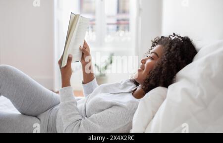 Frau, die im Bett liegt und ein Buch liest, Seitenansicht Stockfoto