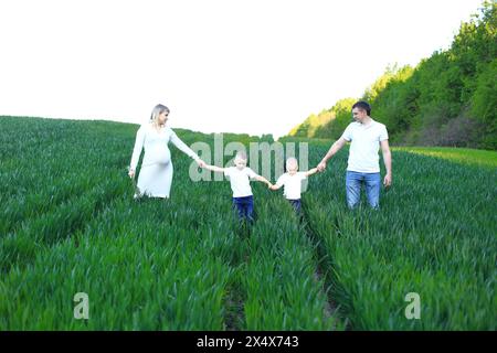 Eine vierköpfige Familie schlendert durch ein üppiges grünes Feld. Das Bild fängt einen Moment der Vorfreude und Einheit ein, während sie die freudige Reise des Exp Stockfoto