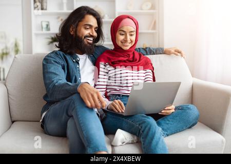 Junges Paar aus dem Osten, das im gemütlichen Zuhause auf einem Laptop surft Stockfoto