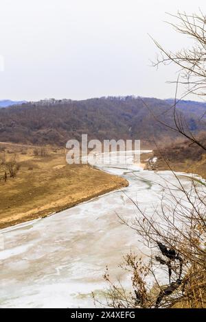 Winterlandschaft des gefrorenen Flusses im Bergtal unter grauem Himmel Stockfoto