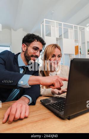 Vertikal. Teamarbeit von Geschäftsleuten, die gemeinsam an einem Unternehmensprojekt arbeiten und kooperieren. Zwei Startup-Kollegen sprechen, während sie einen Laptop am Arbeitsplatz verwenden. Zusammenarbeit mit Kollegen. Hochwertige Fotos Stockfoto