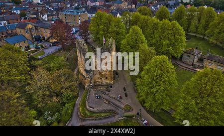 Blick aus der Vogelperspektive auf eine alte Burg, umgeben von üppigen grünen Bäumen in einer malerischen Stadt, mit Menschen, die rund um die Stätte laufen. Stockfoto