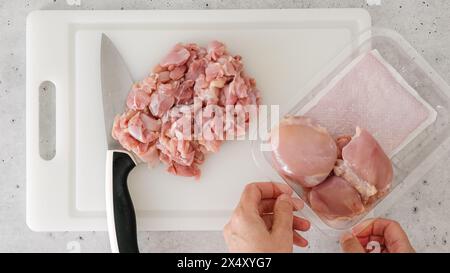 Gehacktes rohes Hähnchenfilet in Nahaufnahme auf einem weißen Kunststoff-Schneidebrett. Der Koch schneidet Fleisch Stockfoto