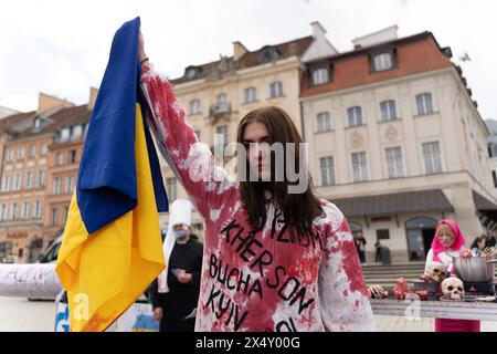 6. April 2024 in Warschau, Polen: Ein Demonstrant in einem blutbefleckten weißen Kleid mit ukrainischen Städten, die von den Russen zerstört wurden, wird während einer Demonstration mit dem Namen „Völkermord-Messe“ mit einer ukrainischen Flagge gesehen. Die Demonstranten veranstalten eine Demonstration namens "Internationale Völkermord-Messe", um die Absurdität der Politik der Europäischen Union zu zeigen, die zwar behauptet, die Ukraine im Krieg zu unterstützen, aber in einigen Gebieten mit Russland Handel treibt. Während des Protests hörten die Teilnehmer russische Musik und tauschten die Knochen der Ukrainer gegen den russischen Rubel aus. (Bild: © Marek Antoni Stockfoto