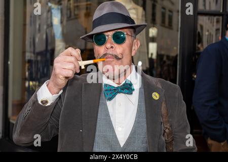 London, Großbritannien. Mai 2024. Ein Gentleman raucht eine Tabakpfeife. Damen und Herren in ihren besten Outfits treffen sich an der Beau Brummell Statue in der Jermyn Street London zum Vierten Grand Flaneur Walk. Quelle: SOPA Images Limited/Alamy Live News Stockfoto