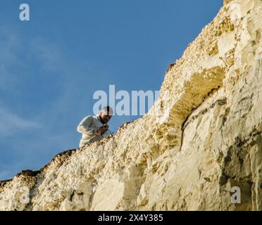 Birling Gap, Eastbourne, East Sussex, Großbritannien. Mai 2024. Ein glorreicher Spätnachmittag und Abend an der Südküste, nicht ganz so viele Besucher wie gestern, aber einige sind wieder sehr nahe am Rand. Dieser Gentleman, etwa 200 Meter hoch, Kameratelefon in der Hand, weiß offensichtlich nichts von der Unterschneidung und Spalte, die sich unter dem Gras und dem Boden versteckt. Die Kreidefelsen entlang dieser Küste sind zerbrechlich und unterschnitten mit häufigen Wasserfällen. Die Warnschilder scheinen unzureichend zu sein und ein Sicherheitsseil vom Beachy Head zum Belle Tout Leuchtturm geht nicht weiter nach Birling Gap. Quelle: David Burr/Alamy Live News Stockfoto