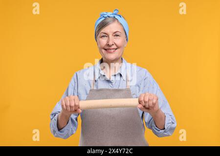 Eine glückliche Hausfrau mit einer rollenden Nadel auf orangem Hintergrund Stockfoto