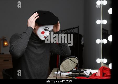 MIME-Künstler, der Baskenmütze in der Nähe des Spiegels in der Garderobe auflegt Stockfoto