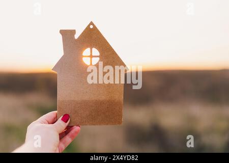 Die Hand des Mannes hält ein hölzernes Haus auf dem Hintergrund verschwommener Gebäude Stockfoto