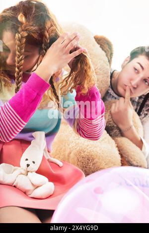 Eine unbeschwerte Interaktion zwischen einer lockigen Frau und einem jungen Mann, beide mit verspielten Requisiten und einem großen Teddybären Stockfoto