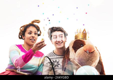 Eine Frau und ein Mann in einer spielerischen Umgebung, umgeben von Ballons und einem großen Teddybären, spielen ein leichtsinniges Spiel Stockfoto