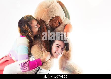 Zwei Freunde oder Geschwister in einer verspielten Umgebung mit einem riesigen Teddybären, einer trägt einen Pelzhut und der andere eine Krone Stockfoto