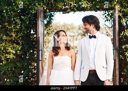 Glückliches Paar, Hochzeit und Händchenhalten mit Liebe durch Eintritt zur Ehe, Unterstützung oder Vertrauen in die Natur. Mann und Frau oder Braut und Bräutigam mit einem Lächeln Stockfoto