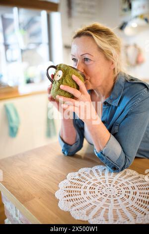 Schöne reife Frau zu Hause, die morgens heißen Tee trinkt. Eine ältere Frau lebt allein und genießt einen friedlichen Wochenendtag Stockfoto