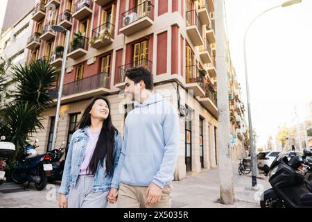 Interaciales Paar, das auf einem Bürgersteig läuft und Hände hält. Junge Männer und Frauen gehen auf der Straße. Stockfoto