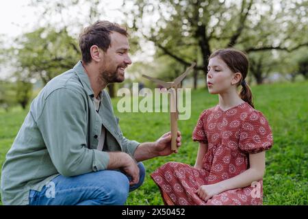 Vater unterrichtet Tochter über erneuerbare Windenergie, nachhaltigen Lebensstil. Draußen im Park stehen, Windkraftanlage halten. Stockfoto