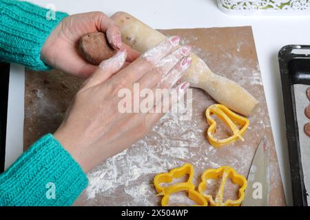 Eine Frau hält einen Klumpen Teig zum Rollen in den Händen. Die Arbeitsfläche ist in Mehl, die Werkzeuge liegen daneben. Lebkuchen kochen. Stockfoto