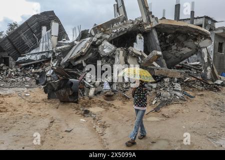 Rafah, Palästinensische Gebiete. Mai 2024. Ein Palästinenser trägt einen Regenschirm, während er neben beschädigten Gebäuden aufwacht. Abed Rahim Khatib/dpa/Alamy Live News Stockfoto