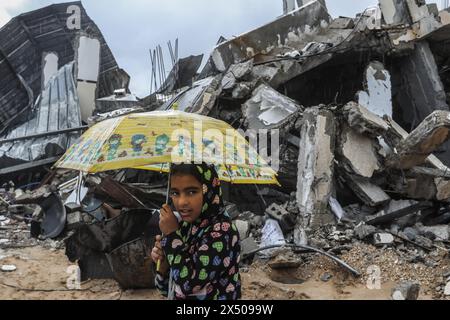 Rafah, Palästinensische Gebiete. Mai 2024. Ein Palästinenser trägt einen Regenschirm, während er neben beschädigten Gebäuden aufwacht. Abed Rahim Khatib/dpa/Alamy Live News Stockfoto