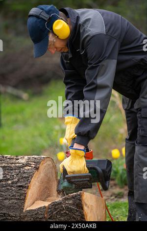 Ein Mann in Uniform schneidet einen alten Baum im Hof mit einer elektrischen Säge Stockfoto