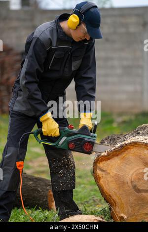 Ein Mann in Uniform schneidet einen alten Baum im Hof mit einer elektrischen Säge Stockfoto