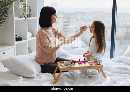Happy Woman trägt Make-up mit Pinsel auf das Gesicht eines kleinen Mädchens. Stockfoto