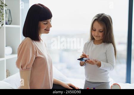 Nahaufnahme Porträt einer kaukasischen Tochter, die Puder auf das Gesicht ihrer jungen Mutter aufträgt. Stockfoto