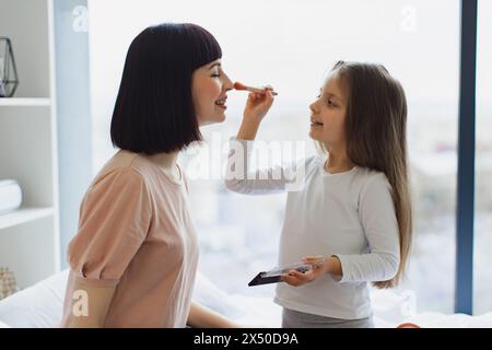 Nahaufnahme Porträt einer kaukasischen Tochter, die Puder auf das Gesicht ihrer jungen Mutter aufträgt. Stockfoto