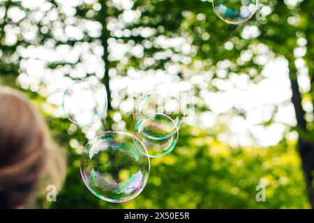 Kind versucht Seifenblasen zu platzen, festliche Atmosphäre, Sonnenstrahlen, Grün, Spaß, das Kind spielt draußen mit Seifenblasen Stockfoto