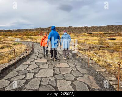 Rückansicht von drei Personen, die auf einem asphaltierten Pfad laufen, Thingvellir Nationalpark, Island Stockfoto