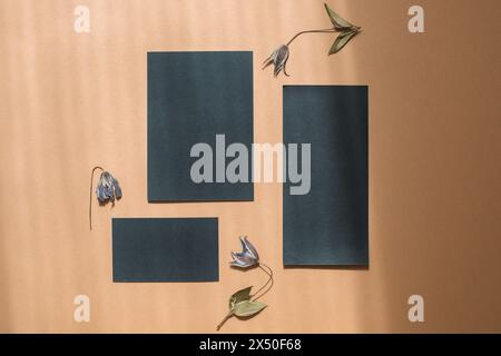 Blick von oben auf leere schwarze Schreibwaren auf einem Holztisch mit Blumen Stockfoto