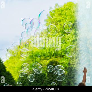 Kind versucht Seifenblasen zu platzen, festliche Atmosphäre, Sonnenstrahlen, Grün, Spaß, das Kind spielt draußen mit Seifenblasen Stockfoto