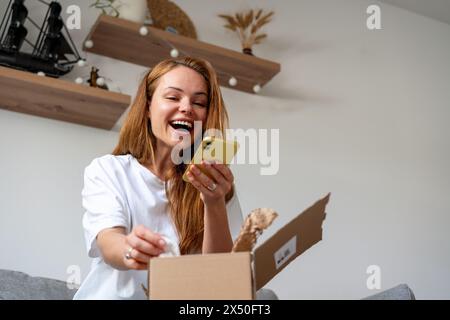 Glückliche Frau, die ein Foto des Kaufs in ihren sozialen Netzwerken postet. Expressversand und zufriedener Verbraucher. Online-Shopping. Stockfoto