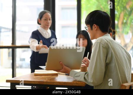 Junger männlicher Student, der dem Professor im Klassenzimmer Projekt auf Laptop zeigt Stockfoto