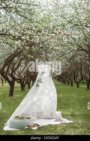 Weißes Zelt, Kissen, Essen und Getränke auf einer Picknickdecke in einem Apfelgarten in voller Blüte, Weißrussland Stockfoto