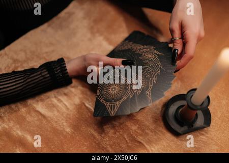 Von oben geschnittene Aufnahme eines unwiedererkennbaren, außerirdischen Glücksspielers, der im Licht brennender Kerzen Tarot-Karten zusammensetzt. Geheimnisvoller Hellseher Stockfoto