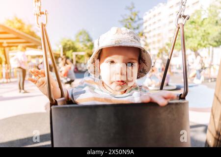 Porträt eines neun Monate alten Babys, das sich auf einer Schaukel im öffentlichen Park amüsiert Stockfoto