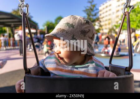 Porträt eines neun Monate alten Babys, das sich auf einer Schaukel im öffentlichen Park amüsiert Stockfoto