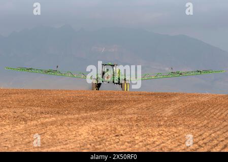 Westkap, Südafrika. April 2024. Traktor mit Auslegerarmen verlängertes Spritzen von Wasser, bevor eine Bohrmaschine Rapssamen auf fa pflanzt Stockfoto