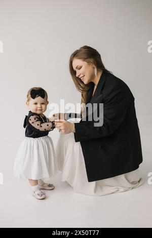 Eine glückliche Frau hält ein lächelndes Mädchen in schwarz-weißer Oberbekleidung Stockfoto